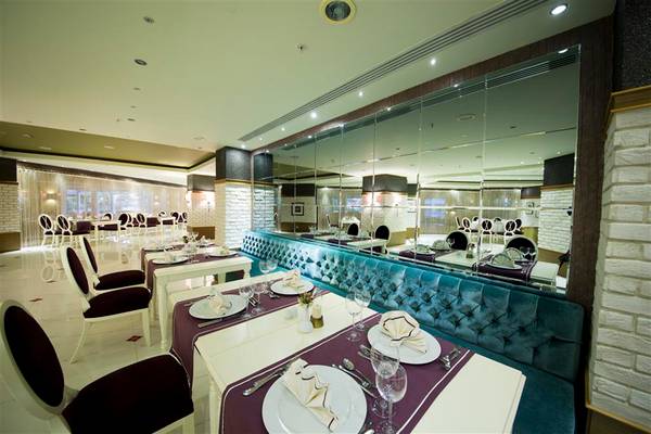 Innenansicht eines Restaurants im Limak Lara De Luxe Hotel & Resort mit gepolsterten Bänken und gedeckten Tischen.