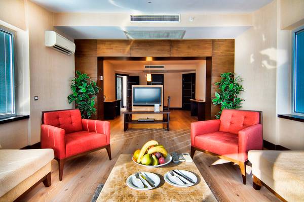 Innenansicht eines Hotelzimmers mit roten Sofas, einem Tisch mit Obst und einer Fernseher.