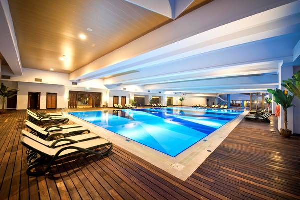 Innenpoolbereich des Limak Lara De Luxe Hotel & Resort mit Loungeliegen und Pflanzen.