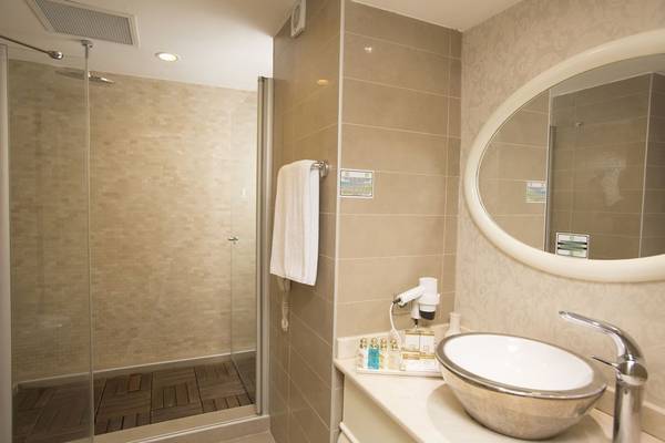 Ein Badezimmer in der Fame Residence Kemer & Spa mit einer Dusche, einem Waschbecken und einem ovalen Spiegel.