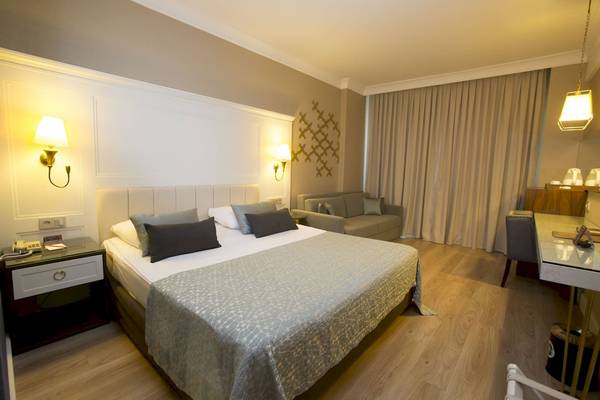 Innenansicht eines Hotelzimmers von Fame Residence Kemer & Spa mit Bett, Sofa und Schreibtisch