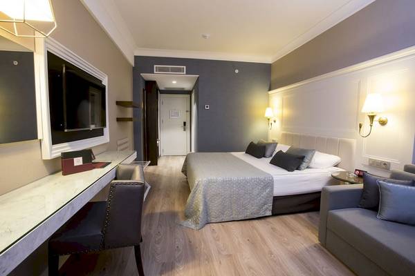 Ein elegantes Hotelzimmer mit einem Bett, einem Schreibtisch, einer Couch und einer Fernsehwand.