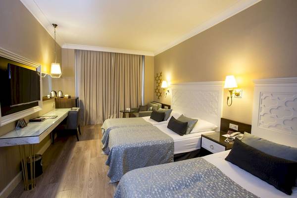 Zimmer im Fame Residence Kemer & Spa mit drei Betten, Schreibtisch und Fernseher.