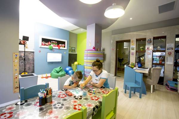 Ein Zimmer mit bunten Wänden, einem Tisch und Stühlen, an dem eine Frau und ein Junge malen.