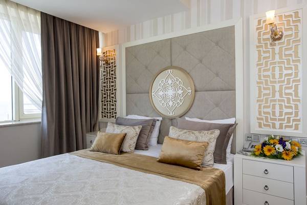 Suite-Bett im Fame Residence Kemer & Spa mit gepolsterter Wand und Blumenvase.