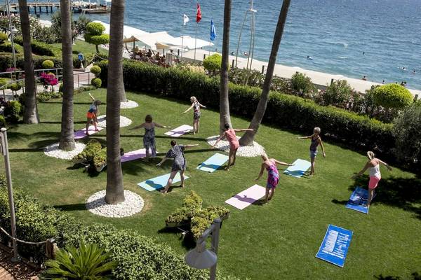 Yoga-Kurs im Garten vor dem Fame Residence Kemer & Spa mit Teilnehmerinnen und Blick aufs Meer.