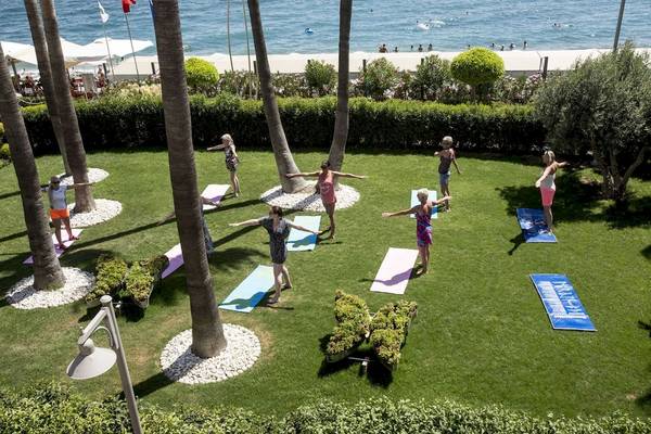 Gruppe von Frauen, die Yoga im Garten des Fame Residence Kemer & Spa Hotels praktizieren.