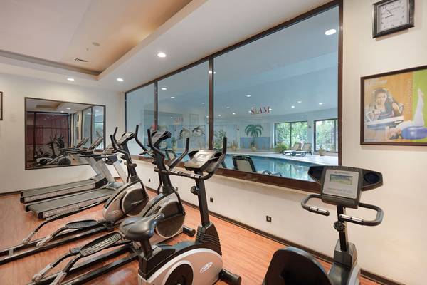 Innenansicht des Fitnesscenters im Siam Elegance Hotel mit Blick auf eine Reihe von Cardiogeräten und einem Pool.