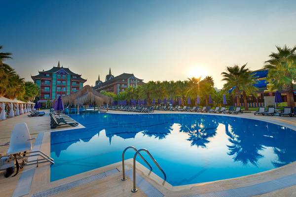 Außenpool des Siam Elegance Hotels & Spa bei Sonnenuntergang mit Lounge-Stühlen und Palmen
