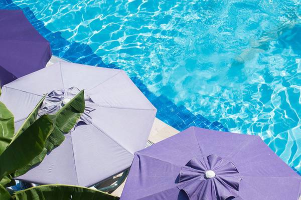 Außenpool des Siam Elegance Hotels & Spa mit mehreren violetten Sonnenschirmen und blauem Wasser.