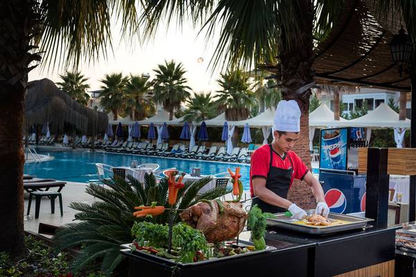 Ein Koch bereitet ein gegrilltes Huhn auf einem Grill vor dem Swimmingpool des Siam Elegance Hotels zu.