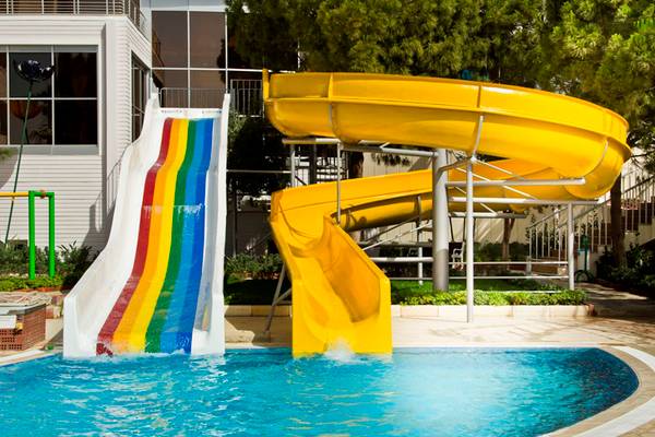 Schwimmbad mit bunter und gelber Wasserrutsche im Freien neben einem Gebäude.