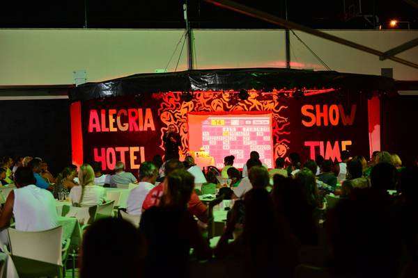 Publikum vor einer Bühne mit der Aufschrift 'Alegria Hotel' und 'Show Time' während einer Veranstaltung.