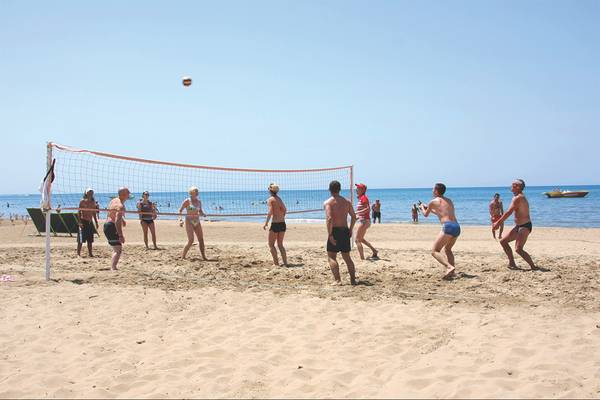 Gruppe von Menschen spielt Volleyball am Strand, im Hintergrund ist das Meer zu sehen.