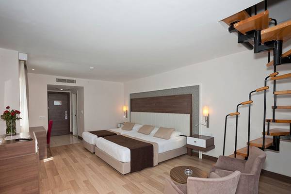 Innenansicht eines Doppelbettzimmers im Side Mare Resort & Spa mit zwei Betten, einem Schreibtisch, Stühlen und einer Treppe.