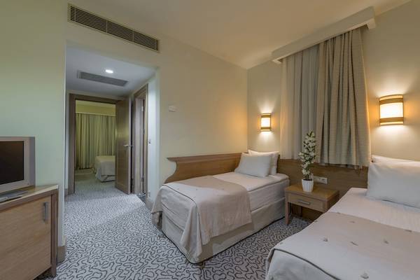 Innenansicht des Dobedan Beach Resort Comfort Zimmers mit zwei Betten, Fernseher, Nachttisch und Eingang zur anderen Kammer.