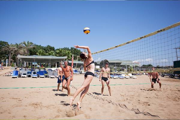 Gruppe von Spielern spielt Volleyball am Dobedan Strand, mit Netz und Schatten im Sand.
