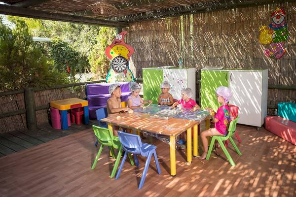 Kinder sitzen an einem Basteltisch im Freien und tragen Plastikschürzen, um ihre Kleidung zu schützen.