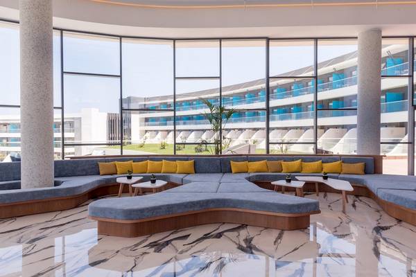 Innenansicht der Lobby im Lyttos Mare Hotel mit geschwungenen Sofas, runden Tischen und großen Fenstern.