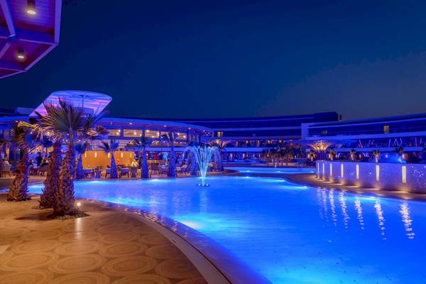 Nachtansicht des Hotel Lyttos Mare mit beleuchtetem Swimmingpool und umliegenden Palmen.