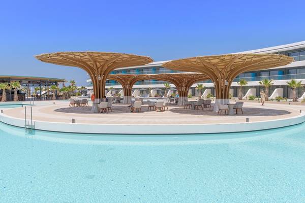 Lyttos Mare Hotel Poolbereich mit großen Bambusschirmen und Tischen im Freien.