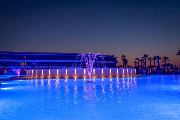 Nachtansicht des beleuchteten Pools des Lyttos Mare Hotels mit Palmen im Hintergrund