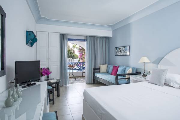 Innenansicht eines Zimmers im Veggera Hotel mit einem großen Bett, einem Balkon und einem Wohnzimmerbereich.