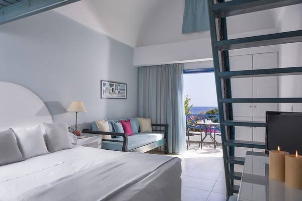 Innenansicht eines Zimmers im Veggera Hotel mit Bett, Couch, Lampen und Meerblick.