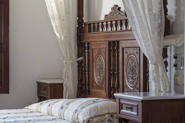 Bett im Veggera Hotel mit kunstvoll geschnitztem Kopfteil und weißen Vorhängen