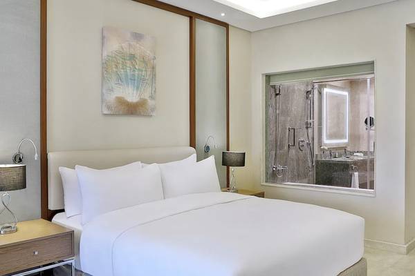 Ein elegantes Hotelzimmer im Hilton Hurghada Plaza mit einem Bett, Lampen und einer Aussicht auf ein Badezimmer.