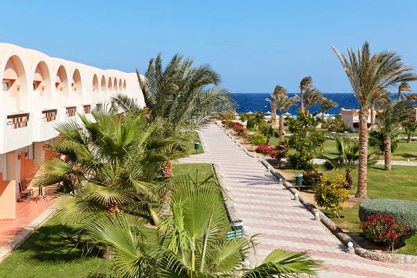 Außenbereich des Three Corners Sea Beach Resorts mit Gehweg, Palmen und Meer im Hintergrund.