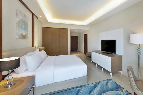 Innenansicht eines Schlafzimmers im Hilton Hurghada Plaza Hotel mit einem großen Bett, Fernseher, Schreibtisch und Lampe.