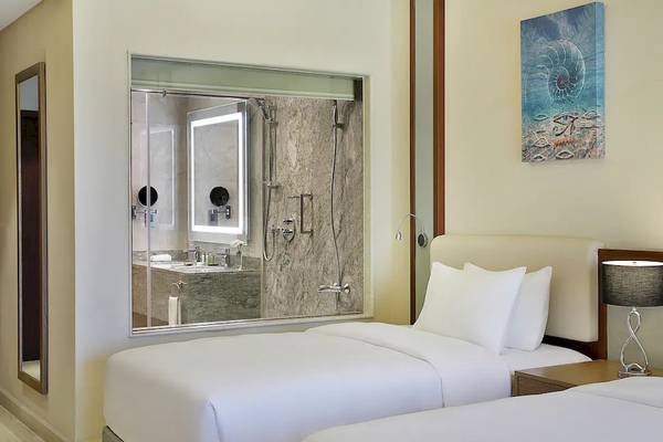 Innenansicht eines Hotelzimmers im Hilton Hurghada Plaza, mit zwei Betten, einem Badezimmer und Kunstwerken an der Wand.