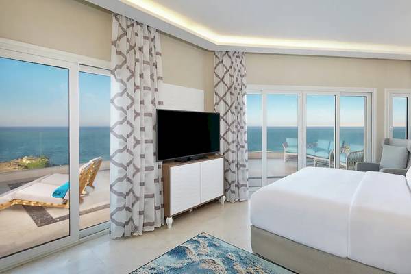 Innenansicht eines Zimmers im Hilton Hurghada Plaza mit Meerblick, inklusive Fernseher und Balkon mit Lounge-Sesseln.
