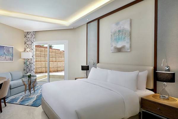 Ein modernes Zimmer im Hilton Hurghada Plaza mit einem großen Bett, Schreibtisch, Sofa und Kunstwerken an der Wand.