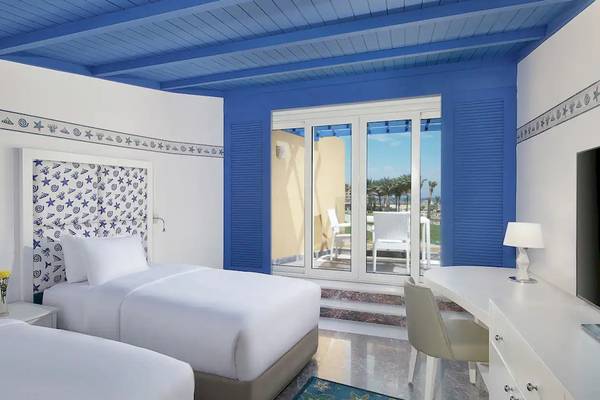 Innenansicht eines Zimmers im Hilton Hurghada Plaza mit zwei Betten, blauen Wänden und einer Terrasse mit Blick auf das Meer.
