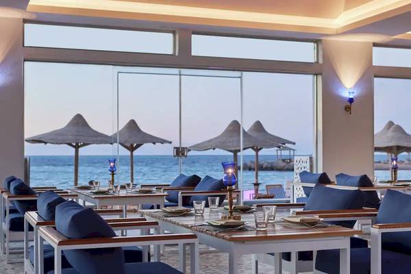 Innenansicht des Restaurants im Hilton Hurghada Plaza mit Blick auf das Meer und mehrere blaue Tische und Stühle.