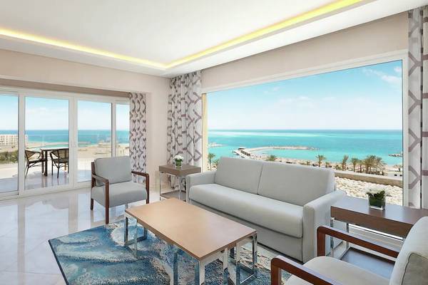 Wohnzimmer des Hilton Hurghada Plaza mit Blick auf das Meer und eine Terrasse mit Tisch und Stühlen.