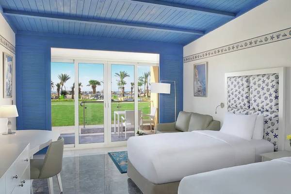 Zimmer im Hilton Hurghada Plaza Hotel mit blauen Wänden und Doppelbetten, Blick auf eine Terrasse mit Garten.