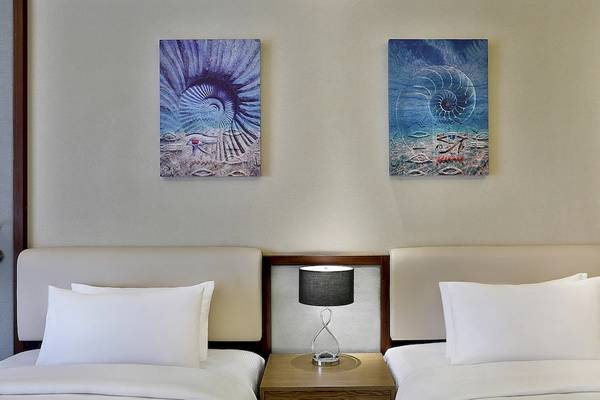 Zwei Betten in einem Hotelzimmer des Hilton Hurghada Plaza, mit Gemälden an der Wand und Nachttischen mit Lampen.