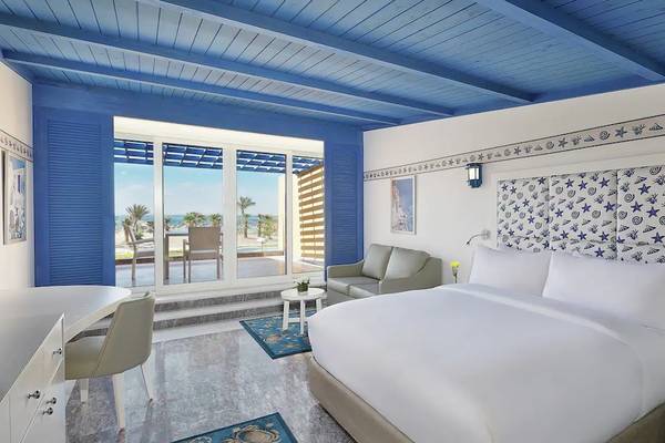 Innenansicht eines Zimmers im Hilton Hurghada Plaza Hotel mit blauem Himmel, weißen Möbeln und Ausblick auf den Strand.