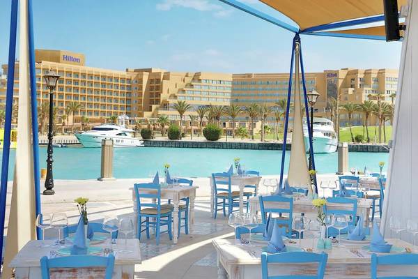 Außenbereich des Hilton Hurghada Plaza Restaurants mit Blick auf das Meer und das Hotel im Hintergrund.