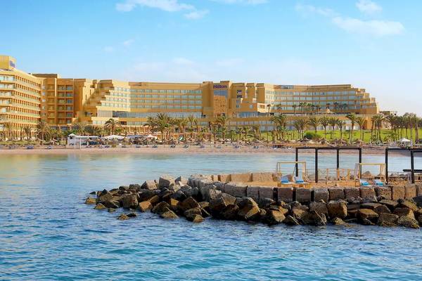 Das Hilton Hurghada Plaza Hotel am Strand mit gelben Gebäuden und vielen Palmen im Hintergrund.