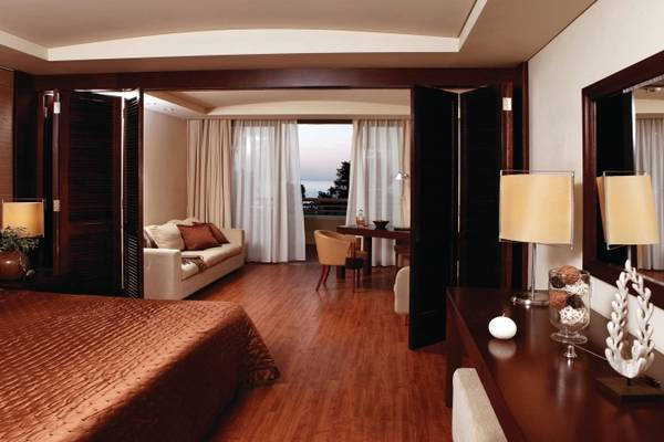 Innenansicht des Schlafzimmers im Porto Carras Meliton Hotel mit Bett, Sofa, Tisch und Fenstern.