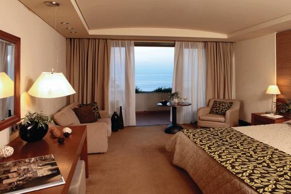 Hotelzimmer im Porto Carras Meliton mit Meerblick, großem Bett, Wohnzimmerbereich und Balkon.