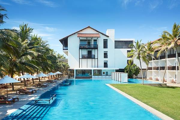 Außenansicht des Jetwing Blue Hotels mit großem Pool, umgeben von Palmen und Liegestühlen.