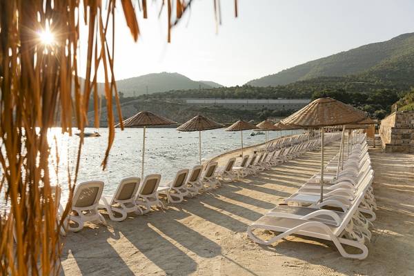 Strand des Duja Bodrum Hotels mit weißen Sonnenliegen und Strohschirmen am Meer