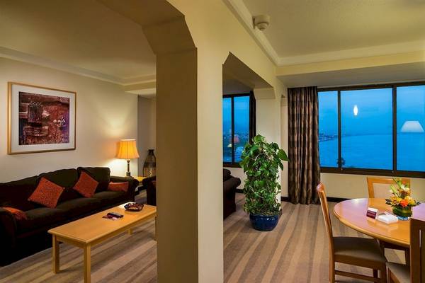 Wohnzimmer im Crowne Plaza Muscat mit Blick auf den Ozean, einem großen Sofa, einem Tisch, einer Lampe und einer Pflanze.