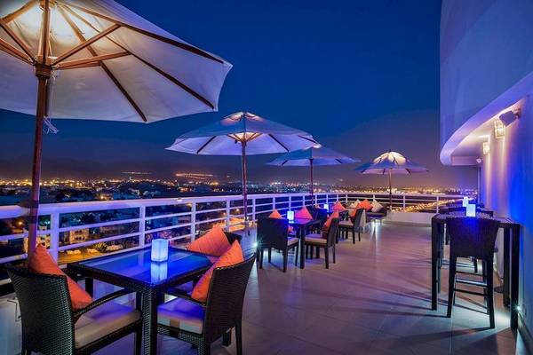 Abendliche Terrasse des Crowne Plaza Muscat mit mehreren Tischen, Stühlen und großen Umbrellas.