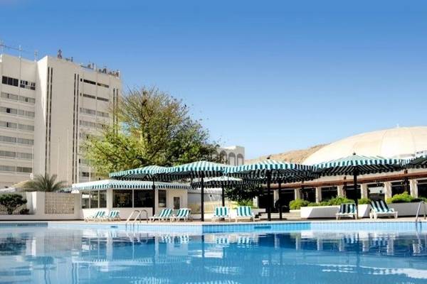 Außenbereich des Al Falaj Hotels mit Swimmingpool, Sonnenliegen und Sonnenschirmen.
